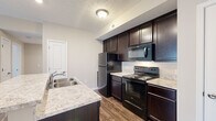 Located at 7405 Long Lake Rd in Columbus, Ohio, this two-bedroom, one-bathroom unit offers a well-organized single-level layout. The kitchen is a standout feature, equipped with rich dark espresso cabinetry, light granite-style countertops, black stainless appliances including a refrigerator, electric range, and over-the-range microwave. A peninsula island with a double sink and bar-height seating separates the kitchen from the living area, creating an open and functional flow. Hardwood-style flooring runs throughout the kitchen and main living areas, lending a clean, modern aesthetic.

The living room is bright and carpeted, with warm neutral-toned walls and a sliding glass door that opens to a private balcony, allowing for natural light and outdoor access. Both bedrooms are carpeted and feature sliding closets with wire shelving for organized storage, along with windows that bring in additional natural light.

The bathroom is well-appointed with a dark vanity cabinet, granite-style countertop, a full tub-shower combination, and tile flooring. A dedicated laundry area with wire shelving and a utility hookup adds everyday convenience. The hallway connects all rooms efficiently, completing this thoughtfully designed residential unit.
