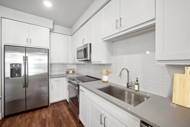 Cocina con acabados de segunda calidad, que incluye electrodomésticos de acero inoxidable, gabinetes blancos, salpicadero de azulejos blancos y encimeras de cuarzo gris. - Avalon Lowry