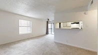 This 2-bedroom, 2-bathroom residence is thoughtfully laid out across a single floor, offering a comfortable and efficient use of space. The open living area is anchored by plush wall-to-wall carpeting, a ceiling fan, and a textured ceiling, while large windows and sliding glass doors leading to a balcony fill the room with natural light and outdoor views. A half-wall pass-through connects the living area to the kitchen, which features light-toned shaker-style cabinetry, white countertops, wood-look flooring, and black appliances including a range, refrigerator, and dishwasher — providing a clean, functional cooking space. The primary bedroom is generously sized with carpeted floors, a window for natural light, and its own dedicated closet equipped with wire shelving for organized storage. The second bedroom is equally well-proportioned with carpeting and a window. Both bathrooms are finished with wood-look flooring, white vanities, and tiled shower-tub combinations. A hallway connects the main living spaces to the bedrooms and bathrooms, and two closets throughout the unit provide ample storage. The overall palette of whites and neutrals creates a bright, clean ambiance throughout.