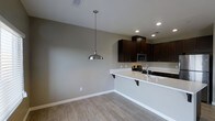 This single-story space showcases a seamlessly integrated kitchen and dining area designed with a clean, modern aesthetic. The kitchen is equipped with rich, dark espresso-toned cabinetry that contrasts sharply against the bright white countertops, creating a striking visual balance. A peninsula with an overhang provides casual seating and doubles as a functional workspace, while a stainless steel sink and gas range add practicality to the layout. A built-in microwave is neatly integrated into the upper cabinetry, maintaining the streamlined appearance.

Recessed lighting illuminates the kitchen area efficiently, while a brushed nickel pendant light hangs above the adjacent dining space, serving as a focal point and providing warm, directed light. The flooring throughout features light wood-look tile, offering both durability and a warm, neutral foundation that complements the overall color palette. Neutral gray walls contribute to the airy, contemporary feel of the space. White baseboards provide a clean finishing detail throughout. The open-concept layout between the kitchen and dining area promotes an easy flow and a sense of spaciousness, making the space both functional and inviting.