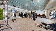 Located in Aurora, CO, this fitness center offers a thoughtfully designed exercise space that combines functionality with modern aesthetics. The room is distinguished by its elegant coffered ceiling finished in a soft teal tone, recessed lighting, and ceiling fans that contribute to a comfortable workout environment. Large windows and glass doors along the exterior walls invite abundant natural light and provide views of the surrounding outdoor area, creating an open and energizing atmosphere.

The space is generously outfitted with a diverse array of equipment to support a full-body workout regimen. Cardio options include treadmills, elliptical machines, stationary bikes, and dedicated cycling bikes arranged for spin-style sessions. A multi-station cable and strength machine anchors the weight training area, complemented by a free weights rack stocked with kettlebells, medicine balls, and dumbbells. Resistance bands and additional accessories are neatly organized on a wall-mounted storage rack.

A floor-to-ceiling mirror spans one wall, visually expanding the space while allowing users to monitor their form. A living green wall panel adds a vibrant, natural accent, and motivational signage reinforces the fitness-forward atmosphere. Wall-mounted flat-screen televisions provide entertainment throughout the workout. The neutral carpet flooring ties the design together, making this facility both practical and visually inviting.
