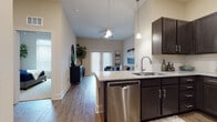 This single-story residence in Austin, Texas, offers a well-designed open-concept layout that seamlessly connects the kitchen, dining, and living areas. The kitchen is a standout feature, outfitted with dark espresso cabinetry extending to the ceiling, granite countertops, stainless steel appliances including a refrigerator, range, microwave, and dishwasher, and a large center island with bar seating and pendant lighting overhead. Wood-look flooring runs throughout the main living areas, adding warmth and continuity.

The living room benefits from soaring vaulted ceilings, a ceiling fan, and French doors that invite natural light while providing access to the outdoors. The space is generous enough to accommodate a comfortable seating arrangement and decorative accents.

The bedrooms are carpeted for comfort and feature large windows with ample natural light. Each room offers meaningful space for furnishings and storage. The bathroom includes a walk-in shower with a clean white surround, wood-look flooring, and neutral wall tones that create a bright, functional space.

Overall, this residence combines modern finishes with a practical layout, making it a well-appointed home in the southwest Austin area.