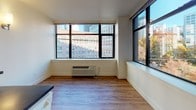 Located on the 8th floor at 201 Yesler Way in Seattle's historic Pioneer Square neighborhood, this single-level residence offers a well-organized layout with a clean, modern aesthetic throughout. Wood-look plank flooring runs continuously across the unit, lending warmth and visual cohesion to every room.

The kitchen is efficiently designed with white cabinetry extending from floor to ceiling, providing ample storage. Dark countertops contrast the light cabinetry, and appliances include a full-size refrigerator, electric range, and dishwasher — all finished in white. Under-cabinet lighting adds functionality to the workspace.

A hallway connects the rooms and is lined with wall-mounted sconce lighting, creating a well-lit passage. The living area is a standout, featuring large, black-framed windows on two walls that frame views of the surrounding Seattle cityscape, including neighboring historic buildings and urban greenery. Natural light fills the room generously throughout the day.

The bedroom is a quiet retreat with its own window offering city views, warm wood-look flooring, and a wall sconce for ambient lighting. The bathroom is clean and functional, featuring a full soaking tub with shower combination and dark countertop vanity. The overall ambiance of the unit is bright, understated, and well-suited to urban living.