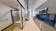 Located at 30 Laurel St in Hartford, CT, this thoughtfully designed industrial-modern unit blends historic character with contemporary finishes. The space showcases an open, elongated layout with light hardwood flooring running throughout, creating a cohesive and airy feel. Exposed concrete ceilings with structural steel beams and columns celebrate the building's industrial heritage, while crisp white walls and modern lighting provide a clean, updated contrast.

The kitchen is outfitted with sleek gray cabinetry, a dark stone countertop with a striking blue backsplash, a built-in electric cooktop, and a wall oven — offering a refined and functional cooking area. A cable-railing staircase and open mezzanine overlook connect the levels, adding architectural depth and visual interest.

The bathroom features a frameless glass sliding door that opens to a fully tiled walk-in shower with stone-look tile surround and matte black fixtures, lending a spa-like quality. An additional open room highlights a dramatic exposed brick wall with arched windows, flooding the space with natural light and paying homage to the building's storied past.

The hallway efficiently connects all areas, maintaining a logical and unobstructed flow throughout the unit. This space is a strong example of adaptive reuse design, combining raw, historic materials with modern amenities.