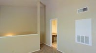 This two-story residence offers a straightforward and functional layout designed for comfortable everyday living. The lower level features smooth, dark hardwood-style flooring that lends a clean, polished look to the main living area. A carpeted staircase with a textured ceiling overhead connects the two floors, providing a smooth transition between living spaces.

The upper level continues with plush carpet flooring, creating a warmer, quieter atmosphere in the sleeping quarters. A bedroom on this floor showcases notably tall ceilings that enhance the sense of openness and airiness, along with a built-in ledge detail along one wall that adds architectural character. A doorway leads directly into an en-suite bathroom, which features tile flooring and wooden cabinetry with vanity storage, offering both convenience and practicality.

Throughout the home, neutral wall tones in soft beige and light gray create a calm, versatile backdrop that pairs well with a wide range of furnishing styles. Textured ceilings are present throughout, adding a subtle design element consistent across both floors. The overall ambiance of the space is understated and move-in ready, with a clean, open feel that invites personalization.