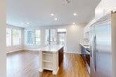 Located at 2500 Vantage Dr in Woodbridge, VA, this well-appointed 2-bedroom, 3-bathroom home offers a thoughtfully designed single-floor layout. The open-concept living, dining, and kitchen area serves as the heart of the home, bathed in natural light from large, wrap-around windows that offer outdoor views. The kitchen is outfitted with stainless steel appliances, white upper cabinetry, a tile backsplash, dark lower cabinets, and a central island with a white quartz countertop and built-in shelving — ideal for both cooking and casual dining. Warm hardwood-style flooring flows throughout the main living areas, complemented by recessed lighting overhead. The bedrooms feature plush carpeting, ceiling fans, and windows that frame natural greenery. The primary bedroom is generously sized and includes a walk-in closet with extensive wire shelving for organized storage. The bathrooms are finished with clean, modern fixtures, including a tiled soaking tub and shower combination, a floating vanity with a white countertop, and hardwood-style flooring. Additional spaces include a combined bathroom and laundry room, a utility room, and multiple closets throughout, ensuring ample storage across the entire home.