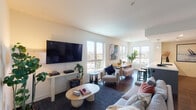 This well-appointed single-floor residence offers a thoughtfully designed open-concept layout that seamlessly connects the main living spaces. The living room is bright and welcoming, lined with multiple large windows that frame outdoor views and fill the space with abundant natural light. Dark hardwood floors run throughout, providing a warm contrast to the crisp white walls.

The kitchen is a standout feature, showcasing dark gray cabinetry, a geometric-patterned tile backsplash, stainless steel appliances including a gas range and French door refrigerator, and a generous island with a white countertop and matte black fixtures. A linear pendant light above the island adds a contemporary touch.

The primary bedroom is generously sized, featuring direct access to an en-suite bathroom with a stylish vanity and a dedicated walk-in closet with dual hanging rods and ample shelving. A second bedroom offers its own natural light through a large window. Both bathrooms are finished with wood-look flooring, modern vanities, and clean white fixtures — one featuring a tiled tub-shower combination. The overall aesthetic is clean, modern, and cohesive throughout.