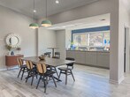 Located at 3200 Oakwood Village Lane in Atlanta, Georgia, this single-floor community clubhouse delivers a polished, modern aesthetic rooted in mid-century design sensibilities. The open-concept layout seamlessly connects multiple functional zones, creating a spacious and welcoming environment throughout.

The main lounge area is anchored by a striking navy blue accent wall adorned with geometric panel molding, vaulted ceilings, and a ceiling fan — lending the space an elevated, residential feel. Light wood-look tile flooring runs throughout, enhancing the sense of openness and tying the rooms together cohesively.

A second lounge zone features bold yellow armchairs, a leather sofa, and a dark wood credenza, all arranged beneath a sculptural brass chandelier and track lighting. Large windows dressed with flowing linen curtains flood the space with natural light and provide views to the exterior. Abstract artwork and curated décor add warmth and visual interest.

Adjacent to the lounges, a dining area centers around a large statement table beneath mint-green pendant lights, with a pass-through window connecting to a well-appointed kitchenette complete with cabinetry and a beverage refrigerator. A co-working area with individual desk stations rounds out the space, offering a productive setting for residents. Together, these zones create a versatile, inviting clubhouse suited for socializing, working, and relaxing.