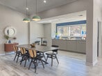 Located at 3200 Oakwood Village Lane in Atlanta, Georgia, this single-floor community clubhouse delivers a polished, modern aesthetic rooted in mid-century design sensibilities. The open-concept layout seamlessly connects multiple functional zones, creating a spacious and welcoming environment throughout.

The main lounge area is anchored by a striking navy blue accent wall adorned with geometric panel molding, vaulted ceilings, and a ceiling fan — lending the space an elevated, residential feel. Light wood-look tile flooring runs throughout, enhancing the sense of openness and tying the rooms together cohesively.

A second lounge zone features bold yellow armchairs, a leather sofa, and a dark wood credenza, all arranged beneath a sculptural brass chandelier and track lighting. Large windows dressed with flowing linen curtains flood the space with natural light and provide views to the exterior. Abstract artwork and curated décor add warmth and visual interest.

Adjacent to the lounges, a dining area centers around a large statement table beneath mint-green pendant lights, with a pass-through window connecting to a well-appointed kitchenette complete with cabinetry and a beverage refrigerator. A co-working area with individual desk stations rounds out the space, offering a productive setting for residents. Together, these zones create a versatile, inviting clubhouse suited for socializing, working, and relaxing.