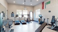 Located at 5870 Labath Ave in Rohnert Park, CA, this single-floor fitness center is part of the Adega Luxury Apartments community and is thoughtfully designed to support a comprehensive workout experience. The space features a clean, modern aesthetic with light-toned walls, durable light-colored flooring, and recessed lighting complemented by ceiling fans that maintain a comfortable environment during exercise.

The cardio zone is well-equipped with multiple treadmills and an elliptical trainer, all positioned in front of large windows fitted with roller shades that allow natural light to filter in while maintaining privacy. An upright stationary bike and an interactive cycling machine round out the cardio offerings.

The strength training area provides a robust selection of equipment, including a multi-function cable and weight machine, a power rack with kettlebells, a full dumbbell rack, and an adjustable workout bench. Full-length wall mirrors line one side of the room, visually expanding the space and allowing users to monitor their form during lifts.

Motivational graphics and wellness-themed typography in bold colors — featuring words like "Focus," "Strength," and "Lift" — add energy to the environment. The Adega Luxury branding is prominently displayed, reinforcing the facility's identity. Overall, the fitness center offers a well-rounded, inviting space for residents seeking a convenient and fully equipped place to pursue their fitness goals.