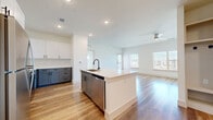 This well-appointed 2-bedroom, 2-bathroom single-story unit offers a thoughtfully designed open-concept layout that seamlessly connects the kitchen and living room. The kitchen serves as the centerpiece, featuring a large island with a built-in sink, stainless steel appliances including a refrigerator, range, and microwave, and a stylish two-tone cabinetry design pairing white upper cabinets with slate-blue lower cabinets. A white subway tile backsplash adds a clean, modern touch. Warm hardwood-style flooring flows throughout the main living areas, while a ceiling fan and multiple windows invite natural light into the living space, which also includes direct exterior access via a glass-paneled door. The bedrooms are carpeted for comfort, each featuring natural light through sizable windows and dedicated closet space. The primary bedroom includes a well-sized walk-in closet. The bathrooms are finished with gray shaker-style vanities, matte black hardware, and tiled tub-shower combinations, maintaining a consistent modern aesthetic. Two closets provide ample storage throughout the unit. The overall design is clean, bright, and contemporary, with a neutral color palette that creates an open and inviting atmosphere.