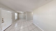 This single-story, 2-bedroom, 1-bathroom home offers a practical and cohesive layout finished with light tile flooring throughout. The living room serves as the heart of the home, featuring neutral gray walls, a textured ceiling, and a window that draws in natural light, creating a bright and open feel. A front entry area welcomes you with a solid white door, an additional window for added daylight, and a flush-mount ceiling light. The galley-style kitchen is well-appointed with white shaker cabinetry, dark granite countertops, a double stainless steel sink, and black appliances including an electric range and refrigerator, all set against clean tile flooring. The primary bedroom offers a comfortable footprint, ceiling fan with integrated lighting, and a window with an outdoor view, while the second bedroom is similarly finished with tile flooring and a paneled closet door. Both bedrooms are supported by two closets featuring built-in shelving for ample organization. The shared bathroom includes a white vanity with dark granite countertop, a mirror with overhead lighting, and white cabinetry. Neutral tones and consistent finishes throughout give this home a clean, move-in-ready appearance.