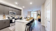 This thoughtfully designed single-floor residence offers an efficient and functional layout encompassing a living room, kitchen, bedroom, and closet. The open-concept kitchen is a standout feature, equipped with dark wood cabinetry with matte black hardware, stainless steel appliances including a side-by-side refrigerator with ice maker, a microwave, range, and dishwasher. A white quartz peninsula with seating for multiple bar stools serves as both a prep area and casual dining space, seamlessly connecting the kitchen to the rest of the living area. Light wood-style flooring runs throughout, lending a clean, contemporary feel. The living room benefits from large windows and a glass door that invite abundant natural light and views of the outdoors, complemented by a ceiling fan overhead. The bedroom is a comfortable, well-lit retreat with a large window framing a green outdoor view, wood-style flooring, and access to an ensuite bathroom via a sliding barn-style door. The ensuite features dark cabinetry consistent with the kitchen's design language. A dedicated closet provides additional storage. Recessed lighting throughout and a neutral color palette create a bright, cohesive ambiance across the entire space.