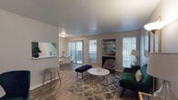 This single-story residence offers a thoughtfully designed layout that balances functionality and comfort throughout its interconnected living spaces. Wood-look flooring extends through the main living and dining areas, complemented by textured ceilings that add subtle dimension to the interior.

The living room serves as the central gathering space, featuring multiple windows that allow natural light to filter in, a built-in display niche with glass shelving, and direct sightlines toward the dining area. A hallway with a louvered vent panel leads visitors into the main living space, reinforcing the unit's efficient use of space.

The dining area is positioned adjacent to the living room and opens directly to an outdoor balcony through a sliding glass door framed by vertical blinds, providing natural light and outdoor access. A pass-through connects this area to the galley-style kitchen, which is outfitted with dark cabinetry, light speckled countertops, a double-basin sink, dishwasher, and refrigerator.

The bedroom offers plush carpeting, a ceiling fan, natural light from a large window, and mirrored sliding closet doors that enhance the sense of space. The bathroom features matching dark cabinetry, a light speckled vanity countertop, overhead storage, and wood-look flooring consistent with the rest of the home.
