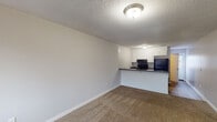 Located at 1528 S Mebane St in Burlington, North Carolina, this single-floor unit offers a straightforward and functional layout designed for comfortable everyday living. The open-concept living area is finished with wall-to-wall carpet and neutral gray walls, creating a clean, versatile backdrop. A textured ceiling with flush-mount lighting keeps the space bright and well-lit throughout.

The kitchen connects seamlessly to the living area via a peninsula counter with a dark laminate surface, providing both workspace and a casual dining option. White cabinetry lines the kitchen walls, offering ample storage, while black appliances — including a Frigidaire refrigerator, electric range, and built-in microwave — add a cohesive, modern contrast. The kitchen features wood-look vinyl flooring, which also extends into the bathroom and laundry areas.

The bedrooms are carpeted and bathed in natural light from windows fitted with horizontal blinds. One bedroom includes a closet with wire shelving for organized storage. The bathroom is clean and functional, featuring a full tub-shower surround, toilet, and wood-look flooring. A dedicated laundry closet with washer and dryer hookups, wire shelving, and hardwood-look floors adds practical convenience to this well-appointed unit.