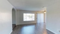 This single-floor residence offers a well-organized layout that balances open living spaces with functional utility areas. The floor plan reveals multiple interconnected rooms arranged to maximize flow and accessibility throughout the home.

The living area serves as the centerpiece of the space, showcasing rich, dark hardwood-style flooring that extends seamlessly throughout. A large picture window and a sliding glass door with vertical blinds allow generous natural light to fill the room, creating a bright and welcoming atmosphere. A ceiling fan with a light fixture adds both practicality and a classic touch to the space. A graceful arched doorway adds an elegant architectural detail, framing the transition between rooms with refined charm.

The textured popcorn ceiling is a consistent design element throughout, complemented by clean white walls and crisp white baseboards that lend the interior a fresh, well-maintained appearance. The kitchen area is positioned centrally within the floor plan, providing convenient access to the surrounding living and dining spaces. Additional rooms, visible in the floor plan, include areas suitable for bedrooms and utility purposes, rounding out a comprehensive and livable layout. Overall, the space presents a clean, comfortable, and functional environment.