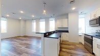 Located on Detroit Avenue in Lakewood, Ohio, this single-floor unit offers a clean, contemporary design with a thoughtfully arranged open-concept layout. The kitchen serves as a central feature, equipped with white shaker-style cabinetry, dark granite-style countertops, a central island with pendant lighting overhead, and a full suite of stainless steel appliances including a refrigerator, electric range, microwave, and dishwasher. Multiple large windows flood both the kitchen and adjoining living area with natural light, providing views of the surrounding Lakewood streetscape. Wood-style plank flooring runs throughout the main living spaces and bedrooms, contributing to a warm, cohesive aesthetic.

The living area is generously proportioned, with a row of tall windows along one wall that amplify the sense of openness. A hallway connects the living spaces to the bedrooms, each of which features wood-style flooring, neutral white walls, and windows offering natural light. The bathroom is finished with large-format tile flooring, a white vanity with dark countertop, a mirror, and a tub-shower combination, maintaining the unit's consistent modern palette throughout.