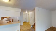 This two-story residence offers a practical and well-organized layout across both levels. The main floor welcomes you through a tiled entryway that flows into the open living area, which features neutral-toned carpet and a window that brings in natural light with views of the surrounding greenery. Adjacent to the living space is a galley-style kitchen, efficiently designed with warm wood cabinetry lining both walls, light countertops, a double basin sink, a white appliance package including a refrigerator and electric range, and a dishwasher. A louvered door closet provides convenient storage within the kitchen. A peninsula counter separates the kitchen from the living area, adding to the open feel of the main floor. The staircase, finished with carpet and white railings, connects the main level to the upper floor. Upstairs, the bedrooms are carpeted and feature white six-panel double closet doors, offering generous storage space. The bathrooms are equipped with tub and shower combinations fitted with curved curtain rods and brushed nickel hardware. Throughout the home, textured ceilings and a clean, neutral color palette create a consistent and understated aesthetic.