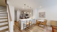 Located at 26 Parsippany Rd in Whippany, NJ, this two-story home offers a thoughtfully designed layout spread across two floors. The main level features an open-concept kitchen, dining, and living area bathed in natural light. The kitchen is equipped with stainless steel appliances, including a gas range, built-in microwave, and French door refrigerator, complemented by gray shaker cabinetry, white quartz countertops, and a central island with bar seating illuminated by sleek pendant lighting. Warm hardwood-style flooring flows throughout the main level, connecting the kitchen seamlessly to the dining nook and a comfortable living room with large windows. A staircase with wood-and-white balustrade leads to the upper floor, where two bedrooms and additional bathrooms are found. The spacious primary bedroom features plush carpeting, bright windows with neighborhood views, and clean white walls. The three bathrooms are finished with neutral tile work and walk-in glass-enclosed showers. A hallway and closet provide practical storage. The home's clean, modern aesthetic is defined by crisp white walls, consistent finishes, and an airy, welcoming ambiance throughout.