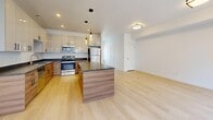 This three-level residence in South Salt Lake, Utah, offers a thoughtfully designed layout with 2 bedrooms and 2 bathrooms. The entry level provides a welcoming introduction to the home, leading up to the main living floor, which hosts the expansive open-concept kitchen and living area. The kitchen is a standout feature, showcasing sleek two-tone cabinetry with light upper cabinets and warm wood lower cabinets, dark granite countertops, a large center island with pendant lighting, and a full suite of stainless steel appliances. Light hardwood-style flooring flows throughout the main level, complementing the bright, airy ambiance. The living area benefits from sliding glass door access to a balcony and multiple windows that fill the space with natural light. The upper floor houses the two bedrooms, each finished with plush carpeting and windows fitted with blinds. The primary bedroom is a generous size with direct access to a well-appointed bathroom. Both bathrooms feature clean white tub-shower combinations, wood-toned vanities with granite countertops, and light wood-style flooring. A closet with built-in shelving adds practical storage. The overall aesthetic is clean, modern, and move-in ready.