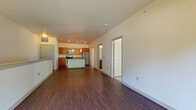This single-floor residence offers a thoughtfully designed open-concept layout that seamlessly connects the living area to the kitchen. Rich hardwood flooring extends throughout the main living spaces, creating a warm and cohesive aesthetic. The living room is generously proportioned, featuring a built-in shelf along one wall and a sliding glass door that opens to a balcony, inviting natural light and outdoor views of surrounding greenery.

The kitchen is a standout feature, showcasing warm wood cabinetry, granite countertops, and a full suite of stainless steel appliances, including a range, microwave, and refrigerator. A central island with a distinctive aqua-colored panel and pendant lighting above serves as both a functional workspace and a visual focal point.

The bedrooms are carpeted for comfort, with large windows that frame outdoor views and fill each room with natural light. The bathroom is finished with tile flooring, a wood vanity with granite countertops, and a full soaking tub with shower combination. Clean white walls and neutral tones throughout the space create a bright, move-in-ready environment with a modern yet approachable character.