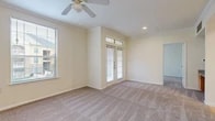 This single-story residence is thoughtfully laid out to maximize functionality and comfort across its well-defined spaces. The living area serves as the heart of the unit, finished with plush neutral carpeting and crowned with crown molding details. A ceiling fan overhead aids in air circulation, while a large side window and elegant French doors with transom glass above flood the space with natural light and provide access to the outdoors.

The kitchen is efficiently designed with warm honey-toned cabinetry extending to the upper walls, granite-look countertops, and durable tile flooring. White appliances, including a full-size refrigerator, electric range, over-the-range microwave, and dishwasher, are neatly integrated into the layout. A closet pantry adds convenient storage, and a pass-through connects the kitchen to the adjacent living area.

The bedroom offers carpeted flooring and direct access to both a generously sized walk-in closet—equipped with multi-tier wire shelving systems—and a private full bathroom. The bathroom features tile flooring, a soaking tub with tiled surround accents, and a clean, functional layout. Overall, the unit presents a practical and comfortable living environment with cohesive finishes throughout.