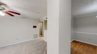 Located at 7872 Taylor Park Rd in Montgomery, Alabama, this single-story residence offers a thoughtfully arranged layout with a neutral color palette throughout. The living room is generously sized, featuring plush carpeting, crown molding, a ceiling fan with light fixture, and a structural column that adds architectural character. A sliding glass door with vertical blinds fills the space with natural light and provides outdoor access. Adjacent to the living area, a dedicated dining room showcases rich hardwood flooring, a pendant light fixture with a chain mount, and a chair rail accent along the walls, creating an inviting atmosphere for meals. The galley-style kitchen is equipped with ample cabinetry in a warm wood tone, a double-basin sink, white appliances including a refrigerator and dishwasher, and hardwood flooring that extends throughout. A hallway connects the bedrooms, each featuring soft carpeting and sliding closet doors offering practical storage. The primary bedroom includes direct access to a bathroom complete with a vanity, mirror with Hollywood-style lighting, and a separate shower-tub combination. A second full bathroom mirrors this layout and is accessible from the hallway. Textured ceilings and crown molding detail the main living areas, adding a classic finishing touch throughout the home.