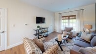 This single-floor residence offers a well-organized layout that balances comfort and functionality across its living, dining, kitchen, bedroom, and bathroom spaces. The living room serves as a focal point of the home, anchored by a striking deep teal accent wall adorned with a large-scale abstract artwork. A plush gray sofa, patterned accent chairs, and a textured area rug contribute to the layered, inviting atmosphere. Natural light filters in through large windows dressed with woven shades and drapery panels, while warm-toned hardwood flooring runs throughout the main living areas.

The kitchen is well-equipped with honey-toned wood cabinetry, stainless steel appliances including a gas range, built-in microwave, and French door refrigerator, complemented by light stone countertops. A generous island provides additional prep space and casual seating. The kitchen flows seamlessly into the dining area, which features a sliding glass door opening to an outdoor deck, allowing natural light to flood the space.

The bedroom is a serene retreat finished with plush carpeting, neutral walls, and large windows framing outdoor greenery. The bathroom features warm wood vanity cabinetry, a light stone countertop, tile flooring, and a walk-in shower area. An in-unit washer and dryer add everyday convenience.
