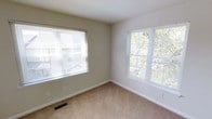 This two-floor space is designed with a practical and comfortable layout. The pictured room exemplifies the overall aesthetic of the interior, showcasing neutral-toned walls in a soft beige finish that create a clean, understated backdrop. Wall-to-wall carpeting in a warm tan shade adds a sense of coziness underfoot throughout the space.

Natural light is a defining feature of this room, with two generously sized windows fitted with horizontal blinds, allowing for adjustable light control. The windows frame views of surrounding greenery, bringing a refreshing outdoor connection to the interior. The room benefits from corner window placement, ensuring light reaches multiple angles throughout the day.

Practical details include a floor-level air vent for climate control, standard electrical outlets positioned at accessible heights, and clean white baseboards that provide a crisp contrast to the carpeted flooring. The walls are smooth and move-in ready.

Spanning two floors, the overall layout of this space offers ample room for flexible living arrangements, with the bright and neutral design making it easy to personalize each area to individual preferences.
