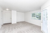 Located at 8804 S State St in Sandy, Utah, this single-floor residence offers a clean, functional layout with a warm and neutral aesthetic throughout. The living area is a standout feature, generously sized with plush wall-to-wall carpeting, a textured ceiling, and an abundance of natural light streaming through multiple large windows dressed with white blinds. A glass-paned door leads directly to an outdoor area, further enhancing the bright and open feel of the space. The bedrooms continue the carpeted theme, each offering clean cream-toned walls, ample floor space, and windows that invite natural light and views of surrounding greenery. The kitchen is well-appointed with white cabinetry, light quartz-style countertops, stainless steel appliances including a refrigerator and range, and wood-look vinyl flooring that adds warmth and durability. A drop-ceiling light fixture provides bright, even illumination throughout the kitchen. The bathroom echoes the same wood-look flooring and features white vanity cabinetry, a tub with a grab bar, and clean white walls, creating a practical yet polished space. Overall, the residence presents a bright, move-in-ready environment with consistent finishes and comfortable living areas throughout.