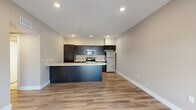 This well-designed 1-bedroom, 1-bathroom unit offers a thoughtful, efficient layout across a single floor. The open-concept kitchen and living area forms the heart of the unit, featuring sleek dark cabinetry, light quartz countertops, a curved peninsula with an integrated sink, and a full suite of stainless steel appliances including a range, microwave, and refrigerator. Recessed lighting illuminates the kitchen, while wood-style plank flooring extends throughout the living area, adding warmth and continuity.

The living room is bright and airy, benefiting from a large sliding glass door that invites abundant natural light and provides outdoor views. A ceiling fan adds comfort to the space. The bedroom is carpeted for a softer feel and includes a ceiling fan, a window for natural light, and access to a generously sized walk-in closet outfitted with multiple hanging rods and additional shelving.

The bathroom features a clean, modern design with large-format tile flooring, a dark wood vanity with a white countertop and undermount sink, and a glass-enclosed shower. A hallway connects the main living spaces, completing this well-appointed, functional single-level unit.