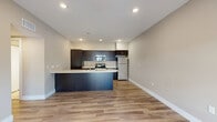 This well-designed 1-bedroom, 1-bathroom unit offers a thoughtful, efficient layout across a single floor. The open-concept kitchen and living area forms the heart of the unit, featuring sleek dark cabinetry, light quartz countertops, a curved peninsula with an integrated sink, and a full suite of stainless steel appliances including a range, microwave, and refrigerator. Recessed lighting illuminates the kitchen, while wood-style plank flooring extends throughout the living area, adding warmth and continuity.

The living room is bright and airy, benefiting from a large sliding glass door that invites abundant natural light and provides outdoor views. A ceiling fan adds comfort to the space. The bedroom is carpeted for a softer feel and includes a ceiling fan, a window for natural light, and access to a generously sized walk-in closet outfitted with multiple hanging rods and additional shelving.

The bathroom features a clean, modern design with large-format tile flooring, a dark wood vanity with a white countertop and undermount sink, and a glass-enclosed shower. A hallway connects the main living spaces, completing this well-appointed, functional single-level unit.