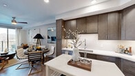 Located at 13220 North Scottsdale Road, this one-bedroom, one-bathroom residence offers a thoughtfully designed open-concept layout that seamlessly connects the kitchen, dining, and living areas. The kitchen is a standout feature, showcasing rich dark-walnut cabinetry extending to the ceiling, crisp white quartz countertops, stainless steel appliances, and a kitchen island that doubles as a casual dining surface. Wood-style flooring runs throughout the main living area, lending warmth and continuity to the space.

The living room is bright and inviting, with a ceiling fan overhead and sliding glass doors that open onto a private balcony, filling the room with natural light. The bedroom offers plush carpeting, a ceiling fan, natural light from dual windows, and a soothing accent wall. A generously sized walk-in closet with multi-tiered shelving and hanging rods provides ample storage.

The bathroom is finished with dark wood cabinetry, white quartz countertops, a backlit vanity mirror, and a full soaking tub with a tiled surround. Light tile flooring completes the clean, contemporary aesthetic. This residence combines modern design with functional comfort in a prime Scottsdale location.