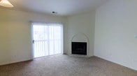 This single-floor space offers a clean, functional layout with a warm and understated aesthetic. The living area serves as the heart of the space, highlighted by a charming fireplace framed with a distinctive arched surround and a tiled hearth, providing a classic focal point to the room. Neutral-toned carpet flows across the floor, contributing to a comfortable and inviting atmosphere.

Natural light fills the room through a large sliding glass door dressed with vertical blinds, offering both brightness and privacy control. The door also provides convenient access to the outdoors, enhancing the sense of openness. The smooth white walls and clean ceiling — fitted with a central air vent — keep the interior feeling bright and airy, allowing the architectural details to stand out without visual clutter.

Overall, the space presents a simple, well-maintained environment with practical features and a neutral palette that serves as an excellent canvas for personalization. The combination of natural light, carpeted comfort, and the fireplace's architectural charm make this a welcoming and livable space.