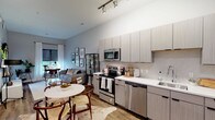Located at 2232 S Grand Blvd in St. Louis, Missouri, this single-floor residence offers a thoughtfully designed open-concept layout with modern finishes throughout. The kitchen is a standout feature, showcasing light gray flat-panel cabinetry, a hexagonal tile backsplash, white quartz countertops, and a full suite of stainless steel appliances including a range, microwave, dishwasher, and French door refrigerator. Wood-look flooring and track lighting enhance the kitchen's contemporary aesthetic, which flows seamlessly into the dining and living areas. The living room benefits from elevated ceilings and a neutral color palette, creating an airy, open atmosphere. The bedroom is a calm retreat with soft gray walls, carpet flooring, and a large window with roller shades and sheer drapes that frame a view of an outdoor patio area. A dedicated laundry area features a stacked washer and dryer unit alongside built-in closet shelving for added storage. The bathroom is clean and functional, finished with wood-look tile flooring, a walk-in glass-enclosed shower, and white vanity cabinetry. Throughout the space, consistent neutral tones and modern design elements create a cohesive, contemporary living environment.