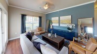 This single-story residence offers a thoughtfully designed layout that balances comfort and functionality. The living room serves as the heart of the home, featuring crown molding, warm neutral walls accented by a bold teal feature wall, and multiple windows that invite natural light and outdoor views. A ceiling fan, decorative pendant lighting, and hardwood-style flooring add to the room's polished character.

The kitchen is well-equipped with rich, dark wood cabinetry extending to the ceiling, granite-style countertops, and a full suite of stainless steel appliances including a range, microwave, and refrigerator. A double sink and pendant lighting over the counter workspace enhance both practicality and style.

The two bedrooms are carpeted for comfort. The primary bedroom features a striking navy accent wall and direct access to the bathroom, while the secondary bedroom benefits from natural light through a large window with decorative curtains.

The bathroom is generously sized, featuring an extended dual-sink vanity with rich wood cabinetry, a large mirror, hardwood-style flooring, and a tub-shower combination — offering both ample storage and a clean, refined aesthetic throughout.