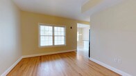This single-floor, 2-bedroom residence offers a thoughtfully designed layout that balances comfort and functionality. The living area is finished with warm, light-toned hardwood flooring that extends throughout, creating a cohesive and inviting atmosphere. Soft yellow-painted walls complement the natural light that pours in through a multi-pane window, lending the space a bright and airy feel.

The living area flows seamlessly into the kitchen, which is visible through an open doorway. The kitchen features tile flooring, a light-colored countertop, and pendant lighting overhead, providing a clean and practical workspace. A full-size refrigerator anchors one side of the kitchen, and the layout allows for efficient use of the available space.

The architectural details throughout are clean and simple, with white trim, smooth ceilings, and minimal ornamentation that give the residence a classic, uncluttered character. The transition between the hardwood and tile flooring at the kitchen threshold is a subtle but functional design choice.

Overall, this residence presents a welcoming environment with a neutral, versatile palette well-suited for a variety of living arrangements, making it an ideal option for those seeking a practical yet comfortable two-bedroom home.