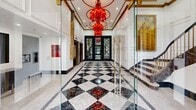 This impressive 620 square foot lobby showcases a harmonious blend of classic and contemporary design elements. The space is dominated by a stunning black and white marble floor arranged in a bold diamond pattern, creating a dramatic visual impact upon entry. Soaring ceilings adorned with gold-trimmed recessed panels and striking red chandeliers add a touch of opulence and grandeur.

The focal point of the lobby is a set of elegant diamond-patterned glass doors, framed by dark metal, which allow natural light to flood the interior. White paneled walls with intricate moldings line the space, contrasting beautifully with the dark marble accents and golden architectural details.

A mezzanine level, visible from the ground floor, features a marble-clad balustrade that overlooks the lobby, enhancing the sense of spaciousness. Modern amenities are seamlessly integrated, including sleek elevators and digital displays, while maintaining the overall classic aesthetic.

The lobby's design elements, including gold-trimmed columns and glass partitions, create a sense of sophistication and refinement. This meticulously crafted space serves as an impressive welcome area, perfectly balancing luxury with functionality in its compact 620 square foot layout.