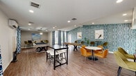 Located at 5584 Ershire Ct in Virginia Beach, Virginia, this single-story community amenity facility is thoughtfully designed to offer a variety of recreational and social spaces under one roof. The layout flows seamlessly across several distinct zones, each with its own character and purpose.

The central lounge area serves as the heart of the space, featuring vaulted ceilings with skylights, recessed lighting, and a striking ceiling fan. A wood-paneled accent wall anchors the room, complemented by a large flat-screen television, a modern pendant chandelier, and wood-look plank flooring throughout. Comfortable seating arrangements create an inviting atmosphere for gathering and relaxation.

Adjacent to the lounge, the game room makes a bold visual statement with a vibrant teal patterned accent wall. It accommodates a shuffleboard table, pool table, arcade machine, and a mix of high-top and standard seating, including warm amber and olive-toned chairs that add a contemporary flair. A smaller seating nook with textured wallcovering and bar-height tables provides an intimate spot nearby.

The catering kitchen features white shaker cabinetry, quartz countertops, stainless steel appliances, and a deep blue subway tile accent wall, with natural light streaming in through large windows.

The fitness center is well-appointed with treadmills, a multi-station cable machine, free weights, and strength equipment, all set atop a vibrant herringbone-patterned floor. Windows along one wall provide natural light and outdoor views.