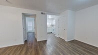 This well-appointed one-bedroom, one-bathroom unit is designed to maximize its efficient footprint across a single floor. The layout connects a living room, bedroom, kitchen, hallway, and bathroom in a logical flow, ensuring practical use of every area.

The living room features durable wood-look plank flooring and crisp white walls, creating a clean, neutral backdrop. A ceiling fan with a built-in light fixture provides both airflow and ambient lighting, while a window fitted with horizontal blinds admits natural light. The open sightlines from the living area toward the kitchen contribute to a more spacious feel.

The kitchen is a notable highlight, featuring white shaker-style cabinetry, light granite countertops, a subway tile backsplash, and white appliances including a refrigerator, range, and dishwasher. Under-cabinet lighting enhances functionality in this well-organized cooking space.

The bedroom is comfortably proportioned, continuing the wood-look flooring and white walls. A window with blinds provides natural light, and a ceiling-mounted light fixture completes the room.

The bathroom includes a full tub and shower combination with floor-to-ceiling tile surround in neutral tones and chrome hardware. Throughout the unit, consistent flooring, white trim, and a clean color palette unify the overall aesthetic.
