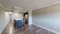 Located at 3020 Reedy Creek Blvd in Kissimmee, Florida, this single-floor unit offers a clean, contemporary layout designed for comfortable everyday living. The open-concept living and kitchen area is anchored by durable wood-style plank flooring that extends throughout the entire unit, complemented by crisp white crown molding and neutral gray textured walls that create a bright, cohesive aesthetic.

The kitchen is well-appointed with a full suite of stainless steel appliances, including a refrigerator, electric range, and built-in microwave. Dark cabinetry provides ample storage, while the kitchen island features a light stone countertop with an integrated sink, offering additional prep space and a natural transition to the living area.

A spacious bedroom receives natural light through a window and connects easily to the rest of the unit via a hallway with access to a louvered closet door. The full bathroom includes a soaking tub and shower combination with tile surround, a stone-top vanity, and brushed dark hardware throughout.

Additional living spaces include a generously sized room with sliding glass doors covered by vertical blinds, allowing for flexible use and natural light control. The unit's entry features a solid paneled front door. Recessed lighting and visible HVAC vents are present throughout, ensuring functional comfort in the Florida climate.