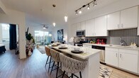 Located at 675 N Grant St in Denver, Colorado, this single-floor residence offers a thoughtfully designed open-concept layout with modern finishes and a cohesive contemporary aesthetic. Wood-style flooring runs throughout, lending warmth and continuity across all areas of the home.

The kitchen serves as a central hub of the living space, outfitted with white shaker cabinetry extending to the ceiling, stainless steel appliances, a textured tile backsplash, and a large center island with bar seating. Pendant lights and track lighting illuminate the workspace, making it both functional and visually striking.

The kitchen flows seamlessly into the living area, where a ceiling fan and sliding glass doors open to a private balcony, bringing in natural light and outdoor views. The living room offers generous wall space and an open, airy feel well-suited for both relaxing and entertaining.

The bedroom features large windows that frame outdoor views, a ceiling fan, and ample natural light. A well-appointed bathroom connects directly to the bedroom, featuring an extended white vanity with quartz countertops, a large mirror, wood-style flooring, and a glass-enclosed shower. The clean, all-white palette throughout the bathroom creates a bright, spa-like atmosphere.
