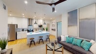This well-appointed single-floor residence offers a thoughtfully designed open-concept layout that seamlessly connects the kitchen, dining, and living areas. The kitchen is a standout feature, showcasing crisp white shaker cabinetry with gold hardware, quartz countertops, a full suite of stainless steel appliances, a striking stainless steel range hood, and a subway tile backsplash. A central island with a white quartz surface provides bar seating and serves as a natural gathering point. Pendant lights and recessed lighting illuminate the space, while light hardwood flooring adds warmth underfoot. The living area features a large ceiling fan, plush carpeting, and a bright window that invites natural light. Two well-sized bedrooms each offer ceiling fans, large windows with blinds and drapes, and access to walk-in closets. The primary bathroom features a backlit vanity mirror, a sleek floating vanity with an undermount sink, and a glass-enclosed shower. The secondary bathroom is finished with large-format tile flooring, an undermount sink vanity, and a full tub-shower combination. Throughout, the space maintains a clean, contemporary aesthetic with neutral tones, modern fixtures, and a cohesive design that balances comfort and style.