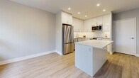 Located at 2911 Bayview in Toronto's North York neighbourhood, this well-appointed 2-bedroom unit offers a thoughtfully designed single-floor layout with a clean, contemporary aesthetic throughout. Light-toned wood-look flooring flows continuously across the living, dining, and bedroom areas, complemented by neutral grey-white walls and crisp white trim.

The living room is generously proportioned, featuring large windows that frame lush, mature treetop views and allow abundant natural light to fill the space. Baseboard heating runs beneath the windows, ensuring year-round comfort. A private balcony with a glass-panel railing extends the living area outdoors, overlooking a verdant, tree-lined backdrop.

The kitchen is a standout feature, outfitted with high-gloss white cabinetry, stainless steel appliances including a refrigerator, stove, and microwave, recessed lighting, and a central island with a clean quartz-style countertop — ideal for both cooking and casual dining. The adjacent dining room provides a dedicated space for meals.

Both bedrooms are well-sized, with the primary bedroom offering a comfortable footprint and a window with garden views. The bathroom is finished in a crisp all-white palette with large-format floor tiles, a soaker tub with shower, and a modern vanity. In-unit laundry with a stacked washer and dryer adds everyday convenience. Five closets provide ample storage throughout.