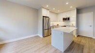 Located at 2911 Bayview in Toronto's North York neighbourhood, this well-appointed 2-bedroom unit offers a thoughtfully designed single-floor layout with a clean, contemporary aesthetic throughout. Light-toned wood-look flooring flows continuously across the living, dining, and bedroom areas, complemented by neutral grey-white walls and crisp white trim.

The living room is generously proportioned, featuring large windows that frame lush, mature treetop views and allow abundant natural light to fill the space. Baseboard heating runs beneath the windows, ensuring year-round comfort. A private balcony with a glass-panel railing extends the living area outdoors, overlooking a verdant, tree-lined backdrop.

The kitchen is a standout feature, outfitted with high-gloss white cabinetry, stainless steel appliances including a refrigerator, stove, and microwave, recessed lighting, and a central island with a clean quartz-style countertop — ideal for both cooking and casual dining. The adjacent dining room provides a dedicated space for meals.

Both bedrooms are well-sized, with the primary bedroom offering a comfortable footprint and a window with garden views. The bathroom is finished in a crisp all-white palette with large-format floor tiles, a soaker tub with shower, and a modern vanity. In-unit laundry with a stacked washer and dryer adds everyday convenience. Five closets provide ample storage throughout.
