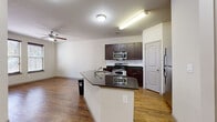 This single-floor, one-bedroom, one-bathroom unit offers a functional and cohesive layout designed for comfortable everyday living. The open-concept kitchen and living area serves as the heart of the space, where a peninsula with dark granite countertops provides both workspace and a casual dining option. The kitchen is equipped with stainless steel appliances — including a gas range, microwave, and refrigerator — complemented by rich, dark espresso cabinetry and a classic white tile backsplash. Warm hardwood-style flooring runs throughout the main living areas, adding continuity and a welcoming feel. A ceiling fan in the living area contributes to air circulation and comfort. The bedroom features plush carpet underfoot, a ceiling fan with light fixture, and a window with blinds that allows natural light to filter in. Two closets offer generous storage, including a walk-in closet with wire shelving and carpeted flooring. The bathroom is appointed with a wide vanity, dark cabinetry with ample under-sink storage, a large mirror, and a glass-enclosed shower. Neutral wall tones throughout create a clean, versatile backdrop suited to a variety of furnishing styles.