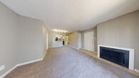 This single-floor residence offers a thoughtfully arranged layout designed for everyday comfort and practicality. The living room serves as the heart of the home, featuring plush wall-to-wall carpeting, neutral taupe-toned walls, and a classic fireplace that anchors the space with warmth and character. A textured ceiling adds subtle dimension, while track lighting overhead provides focused illumination. Tile flooring at the entryway transitions seamlessly into the carpeted living area, creating a natural delineation of spaces. The kitchen is open to the living area via a raised peninsula breakfast bar, making it ideal for casual dining or entertaining. White cabinetry lines the walls, complemented by a stainless steel refrigerator, an electric range, and a microwave. Light wood-look vinyl flooring runs through the kitchen and extends into a dedicated laundry corridor, where an in-unit washer is conveniently tucked away. The bedroom is generously proportioned with soft carpet underfoot and a large window fitted with horizontal blinds, allowing natural light to filter through while maintaining privacy. The bathroom is clean and functional, featuring a full tub-shower combination with tile surround, wood-look vinyl flooring, and a classic white vanity setup.