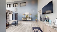 Located at 412 3rd St E in Hastings, MN, this building lobby offers a welcoming and thoughtfully designed communal space across a single open floor. The lobby is distinguished by dramatically soaring double-height ceilings with clerestory windows that flood the interior with natural light, creating an airy, open atmosphere. Light wood-look luxury vinyl flooring runs throughout, complementing the cool blue-gray accent walls that lend a sophisticated, modern character to the space.

The lounge area features a bold geometric patterned accent wall alongside exposed ductwork, lending an industrial-chic aesthetic, while a large decorative clock and curated furnishings — including a leather lounge chair and upholstered bar-height seating — add elegance and comfort. A mirrored gold-detailed console table serves as a striking focal point, dressed with tasteful décor including lush plants, framed artwork, and stylish lamps.

The dining area is bathed in natural light from a bank of large windows overlooking the surrounding streetscape, centered around a round pedestal table with upholstered bar chairs. A built-in counter with granite surfaces and a coffee station provides added convenience. Resident mailboxes are accessible from an adjoining corridor, rounding out the practical amenities of this well-appointed and visually impressive lobby.
