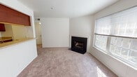 This single-story residence offers a well-organized layout that balances comfort and functionality across its living spaces. The living room serves as the focal point of the home, anchored by a classic wood-burning fireplace with a white surround and black hearth, complemented by neutral carpeting and a window fitted with blinds that allows natural light to fill the room. A pass-through opening connects the living area to the kitchen, enhancing the sense of openness between the two spaces.

The galley-style kitchen is outfitted with rich, dark wood cabinetry providing ample upper and lower storage, light-toned countertops, a stainless steel sink, a dishwasher, and a stainless steel refrigerator. Durable hardwood-style flooring runs throughout the kitchen, contrasting warmly with the cabinetry. A dedicated entry door leads directly from the kitchen area.

The bedrooms are carpeted and feature neutral walls with windows overlooking lush greenery, inviting plentiful natural light. Additional rooms visible in the floor plan provide flexible living options. The bathroom includes a full tub-shower combination with white tile surround and chrome fixtures, maintaining a clean, functional aesthetic throughout.