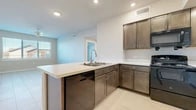 This single-floor unit offers a clean, contemporary design highlighted by consistent light-toned tile flooring throughout. The kitchen serves as a central feature, showcasing rich dark-stained cabinetry with sleek hardware, white countertops, and a full suite of black appliances including a range, over-the-range microwave, refrigerator, and dishwasher. A peninsula with a double-basin sink and pull-down faucet extends into the living area, providing both additional prep space and an open sightline to adjacent rooms. Recessed lighting illuminates the kitchen efficiently.

The entryway is clean and functional, flanked by multiple white panel doors leading to various rooms. Bedrooms feature neutral walls, tile flooring, ceiling fans, and windows with blinds that bring in natural light and exterior views. Closets with built-in shelving provide practical storage.

Both bathrooms maintain the same design language as the kitchen, with dark wood-toned vanities, white countertops, large mirrors, and light fixture bars. One bathroom includes a shower-tub combination, while the other is fitted with grab bars, suggesting accessibility considerations. The overall palette of warm neutrals and dark wood tones creates a cohesive, modern aesthetic throughout.